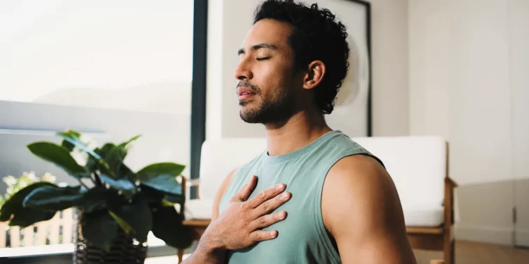Man practicing deep breathing with his hand on his chest to promote better sleep and overall men's health.