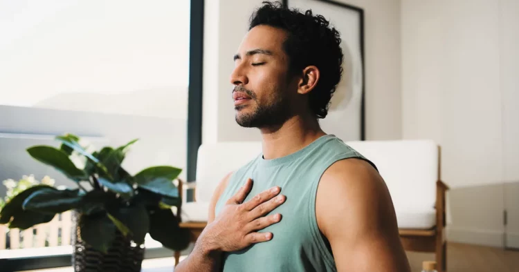 Man practicing deep breathing with his hand on his chest to promote better sleep and overall men's health.